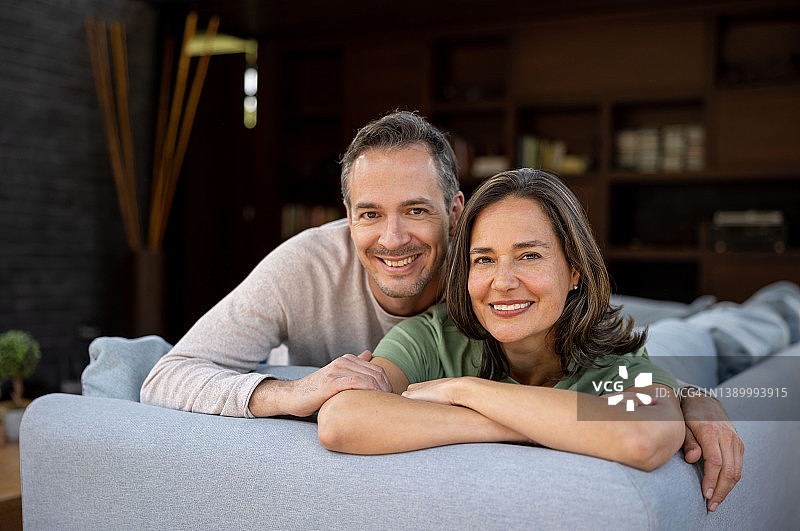 一对幸福的夫妇在家微笑，放松地坐在沙发上看着相机图片素材