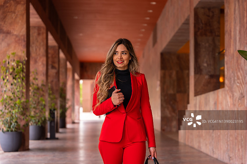 身穿红色西装的年轻白人女商人抵达酒店，带着包和平板电脑出差图片素材