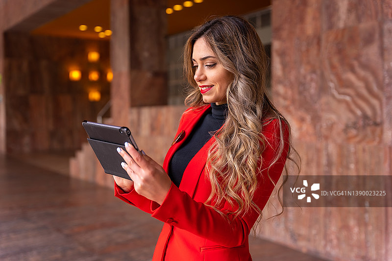 年轻的白人女商人穿着红色西装到达酒店，出差工作，在会议前查看笔记和邮件图片素材