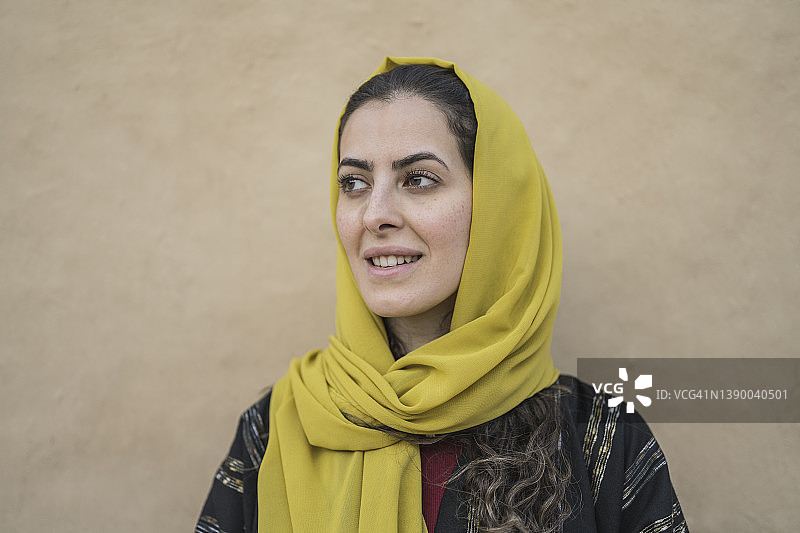 戴着头巾和穿长袍的女人靠在土坯墙上图片素材