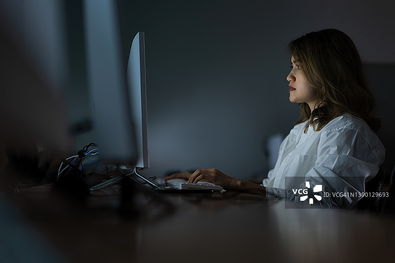 疲惫的年轻亚洲女性在工作办公室中心熬夜，她正在使用台式电脑，承受着压力和截止日期的概念图片素材