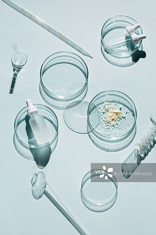 蓝色背景上的实验室玻璃器皿和化妆品玻璃瓶。天然药物、化妆品研究、生物科学、有机护肤品。俯视，平铺。研发概念。图片素材