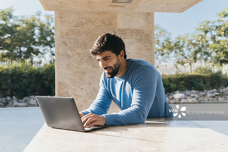 靠墙使用笔记本电脑的微笑年轻人图片素材