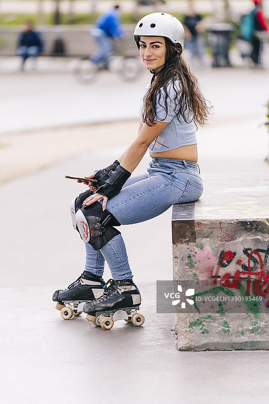 在公园水泥地上坐着的微笑滑旱冰女人图片素材