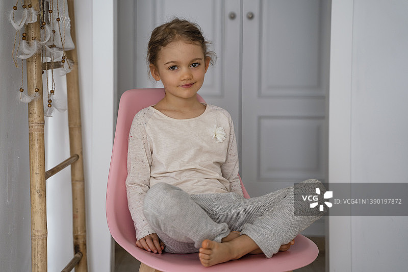 可爱的女孩在家中粉色椅子上盘腿而坐图片素材