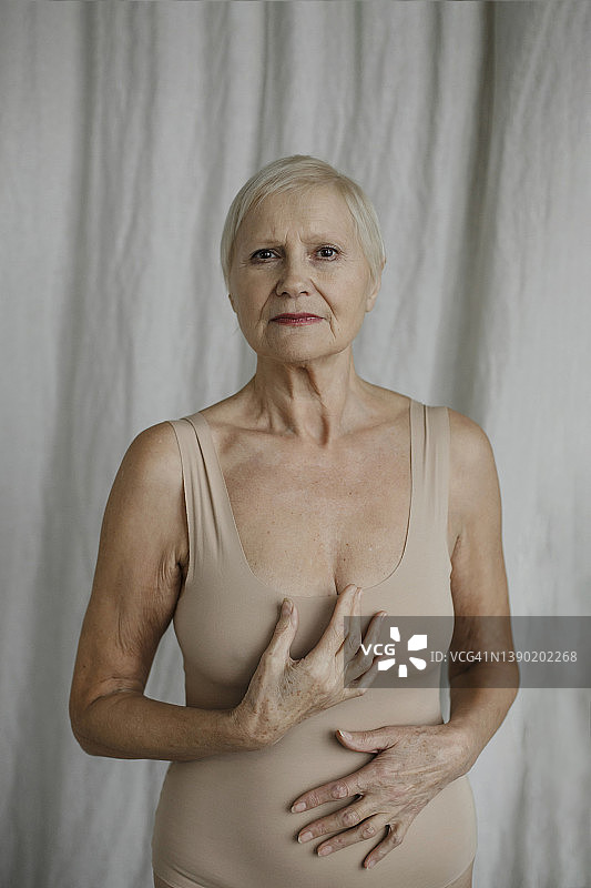 穿着紧身衣站在家里的窗帘前的年长的女人图片素材