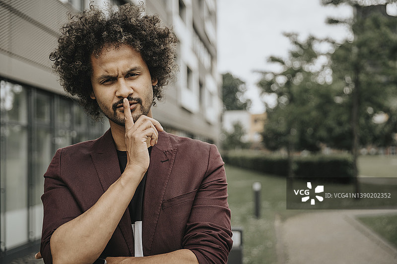 在建筑物旁用手指放在嘴唇上的年轻男人图片素材