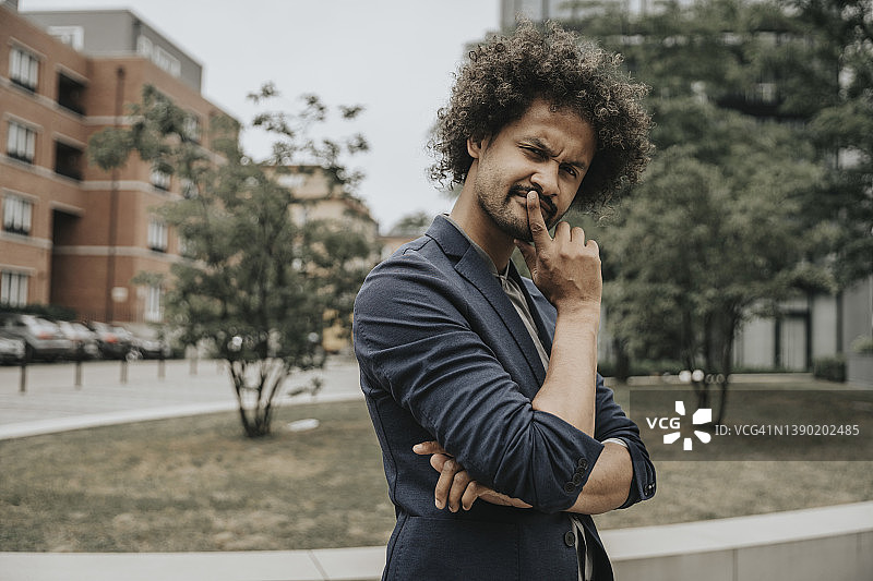 站在现代建筑前，手指放在嘴唇上的持怀疑态度的年轻人图片素材