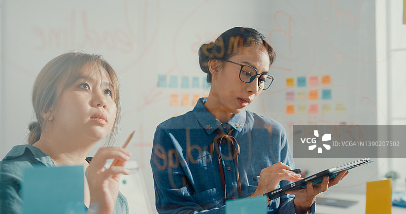 一群穿着时尚休闲的年轻亚洲女商人使用平板电脑，并在彩色便利贴上书写，在创意办公室中开发商业项目图片素材