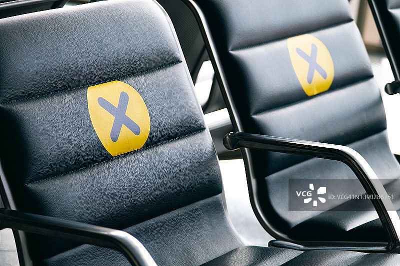 贴在机场椅子上的黄色标志新贴纸，与其他人相隔一个座位，保持距离，预防和防止COVID-19新冠病毒传播风险，隔离和疫情期间的空座位图片素材