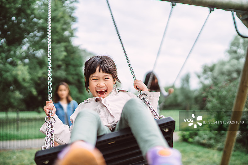 可爱的小女孩在游乐场的秋千上快乐地笑着图片素材