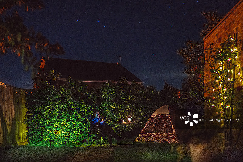 年轻帅气的男人在房子的后院，露营帐篷旁用电子阅读器阅读图片素材