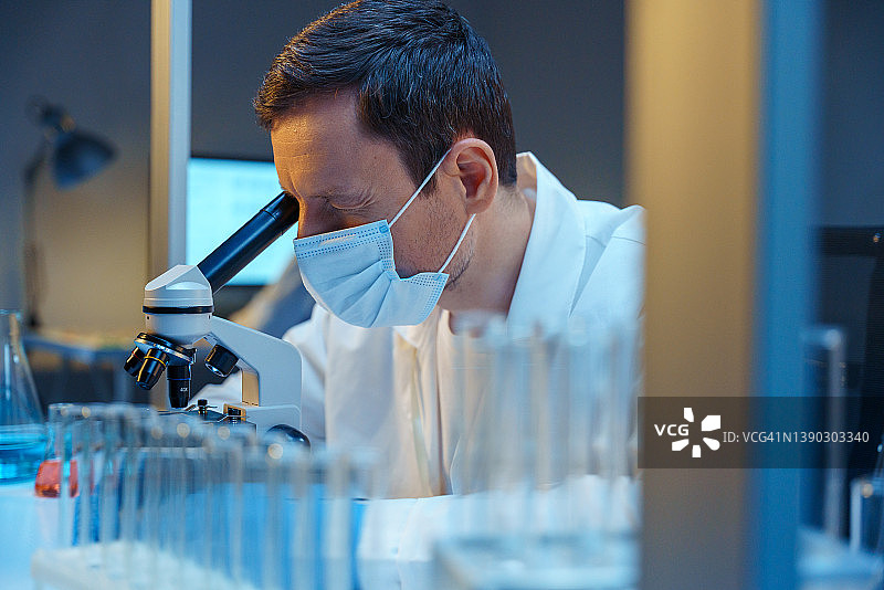 在实验室工作的白人科学家，坐在试管架后的桌子旁图片素材