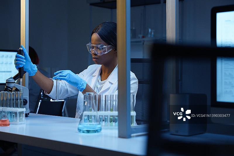 非裔美国女科学家在现代实验室的办公桌前工作，在试管中进行化学反应图片素材