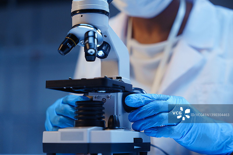 蓝色背景上手持显微镜和戴防护手套的科学家图片素材