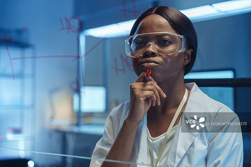 年轻的非裔美国女科学家思考玻璃板上化学反应的解决方案图片素材