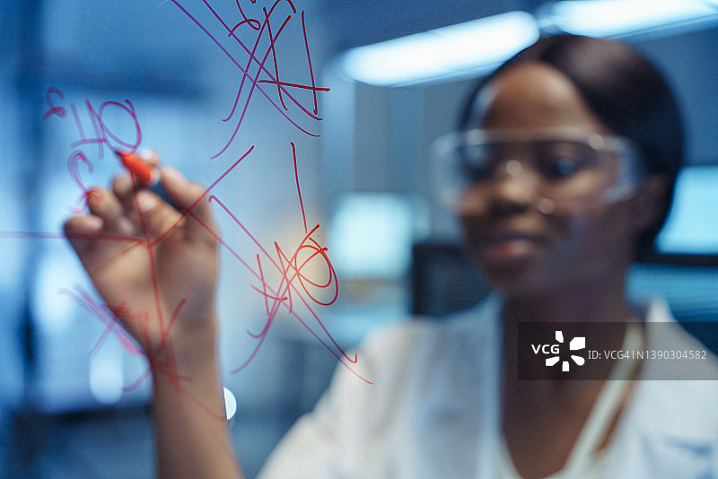 一位年轻聪明的非裔美国人科学家正在现代实验室里，在面前的玻璃板上书写化学反应图片素材