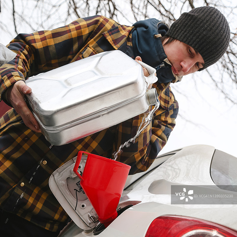 年轻男子用红色漏斗和罐子给汽车加油图片素材
