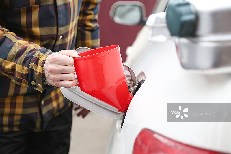 年轻男子用红色漏斗和罐子给汽车加油图片素材
