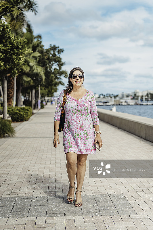 拉丁裔女人走在沿海热带市区，有棕榈树和建筑物图片素材
