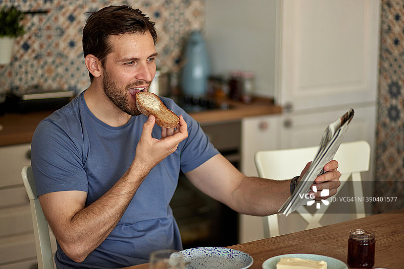 英俊的男人一边吃早餐一边看报纸图片素材
