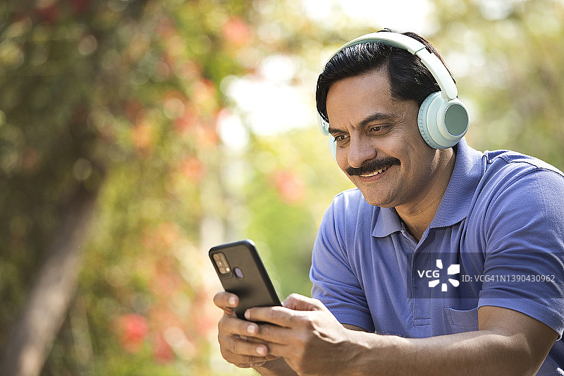 在公园用手机和耳机听音乐的无忧无虑的男人图片素材