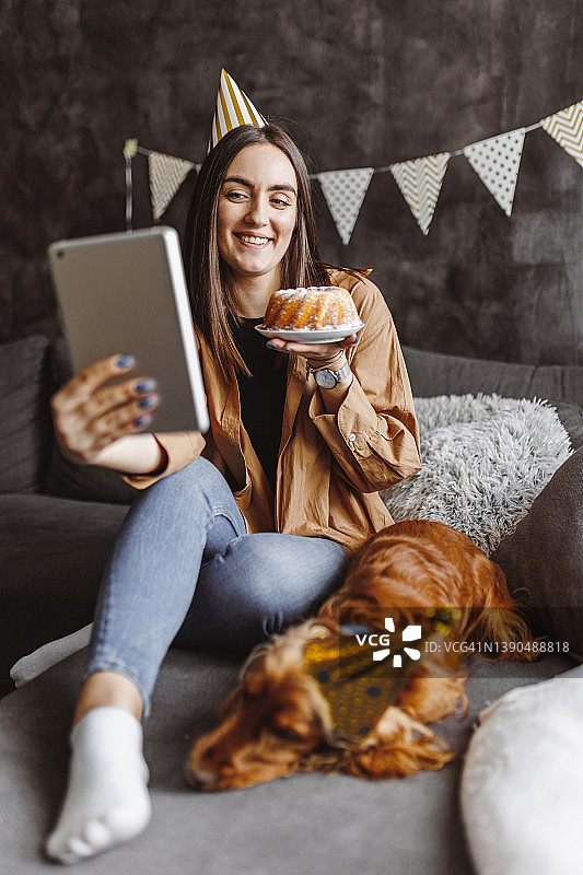快乐的女人和她的狗一起庆祝生日，与朋友进行视频通话图片素材