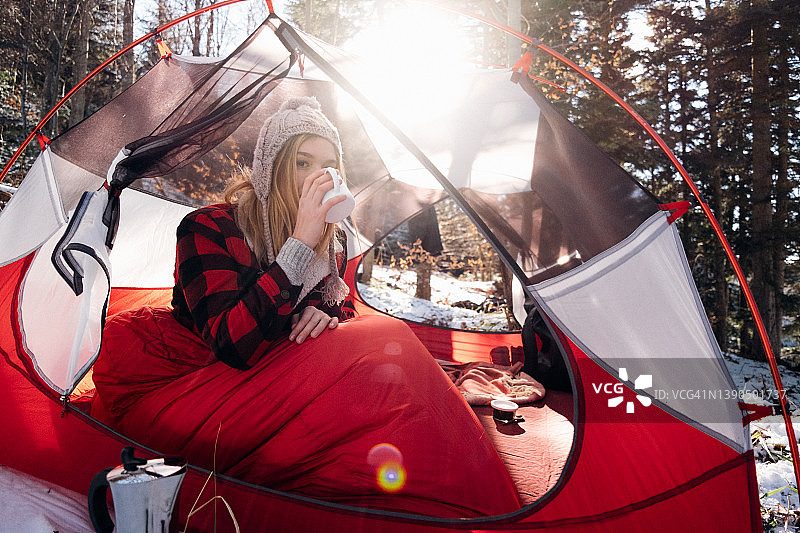 在阳光下的帐篷里用马克杯喝水的女人图片素材