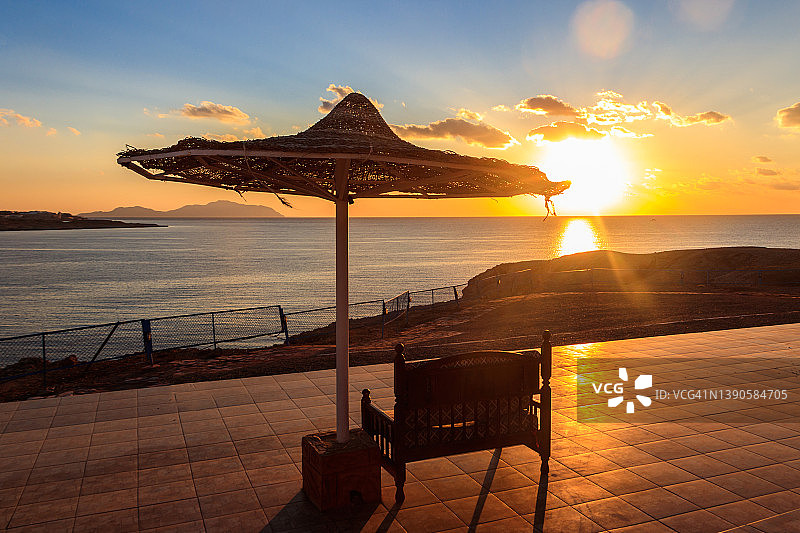海滩遮阳伞下的舒适长椅，日出时分欣赏美丽海景，夏季度假概念图片素材