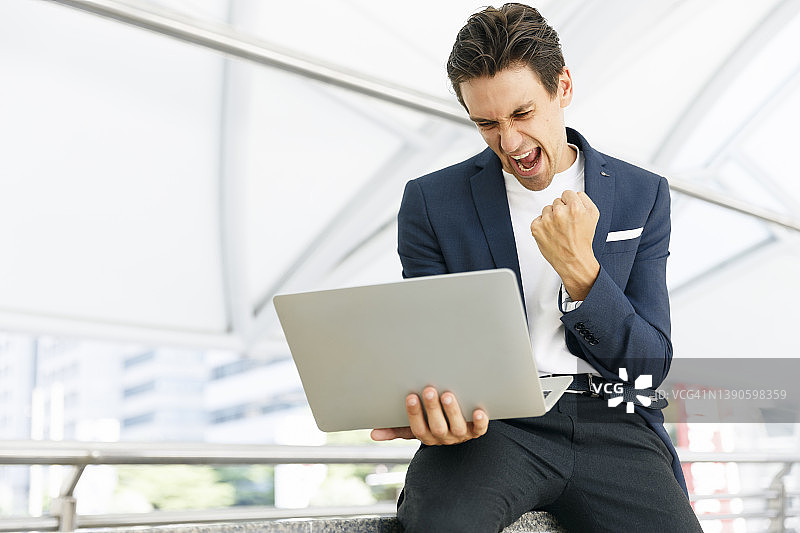 年轻商务人士户外用笔记本电脑，笑容灿烂。图片素材