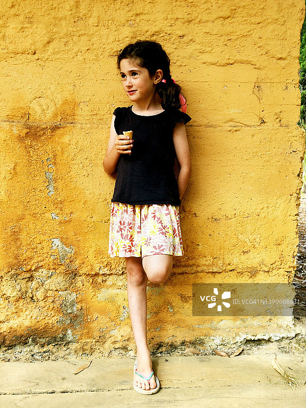 年轻的女孩靠在黄色的墙上图片素材