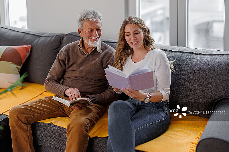 在家中与年轻孙女一起读书的年长的白人男子图片素材