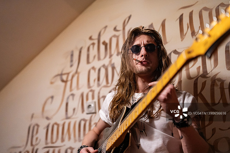 年轻的摇滚音乐家抽着烟弹奏电吉他图片素材