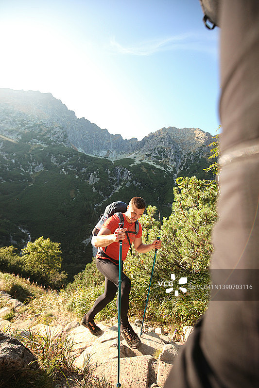 男子在山区岩石小路上用背包和登山杖徒步旅行图片素材