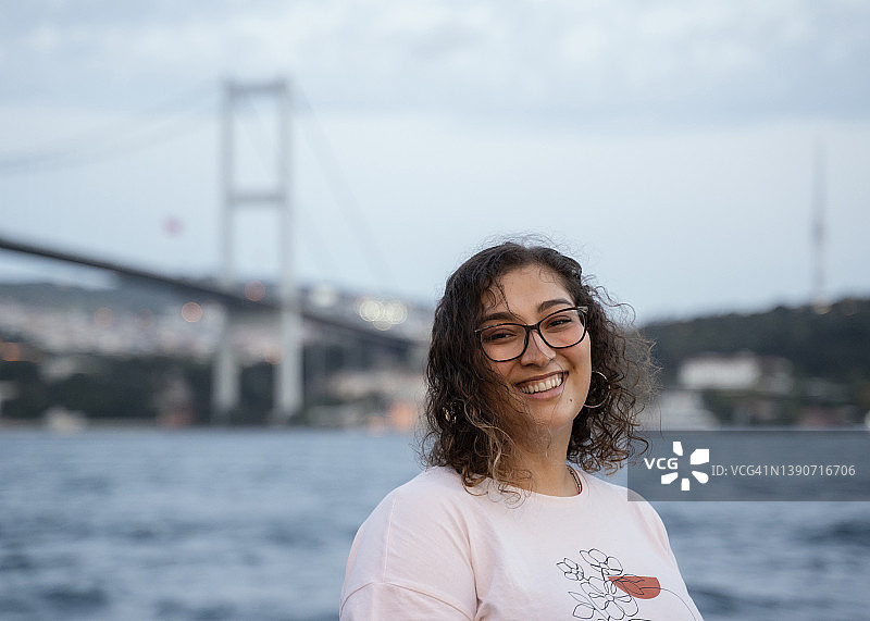 快乐的年轻女孩肖像，背景是伊斯坦布尔博斯普鲁斯海峡大桥图片素材