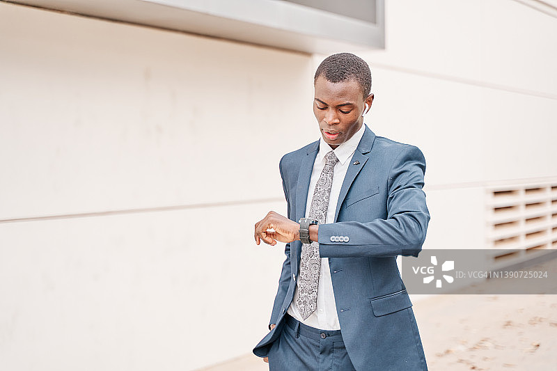 身穿现代西装的年轻非洲裔美国商务男士在城市背景中看手表图片素材