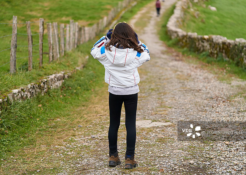 寒冷的冬日，女孩站在城市郊外乡村地区的土路上，穿着夹克和手套图片素材