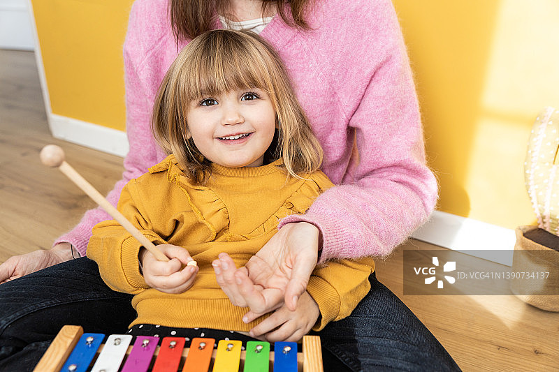 小女孩和妈妈一起学音乐，看着镜头的正面图图片素材