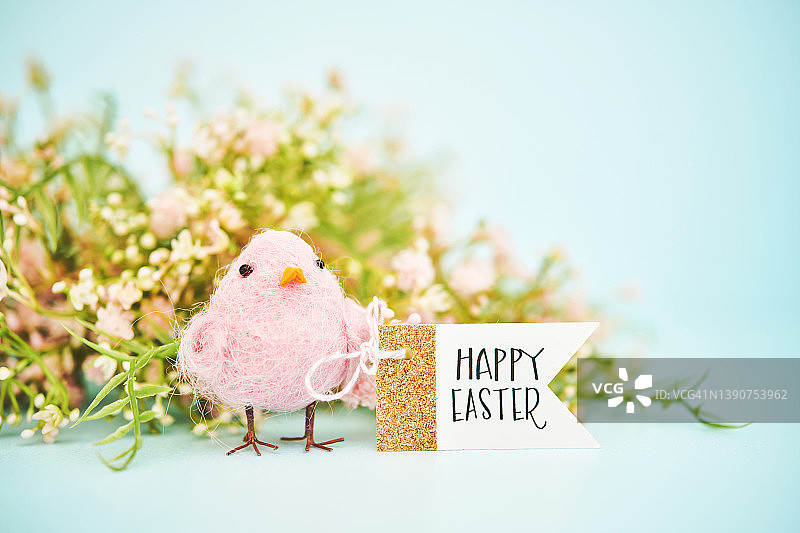 可爱的粉色毛毡鸟，背景是写着“复活节快乐”的牌子和一束春天的花朵图片素材