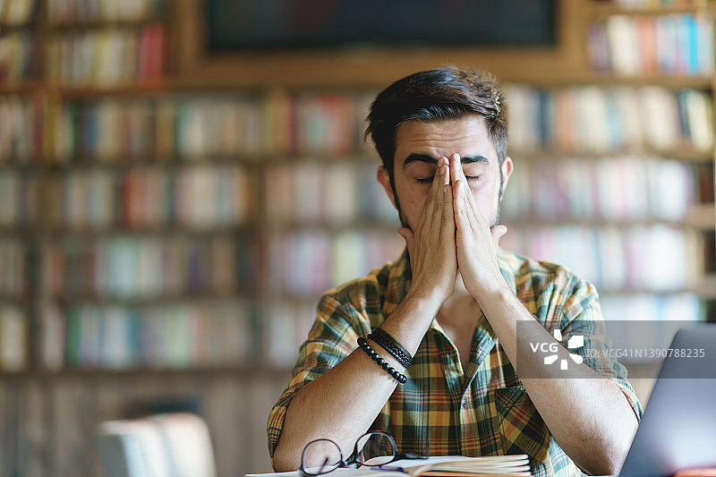 疲惫的年轻男子在图书馆揉眼睛图片素材