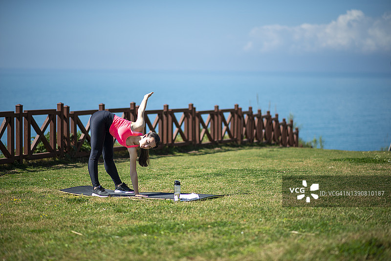 年轻的运动型女人在海边草地上做早操图片素材