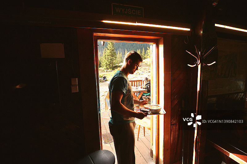 男人端着食物托盘穿过山间小屋的门图片素材
