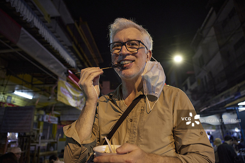 微笑的老年男人在吃街头小吃图片素材