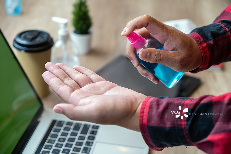 男人在使用笔记本电脑前用消毒喷雾消毒双手的特写图片素材