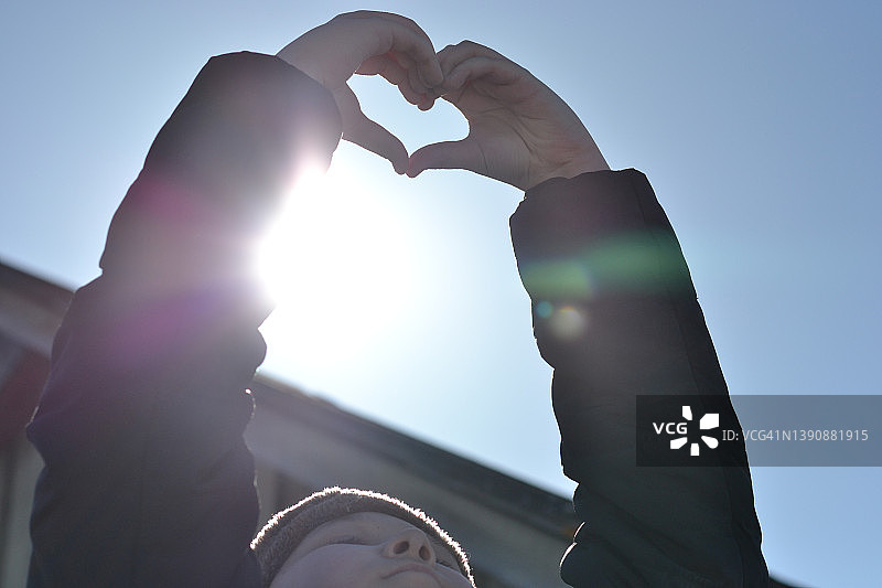 男孩在晴朗的蓝天下用手比心图片素材