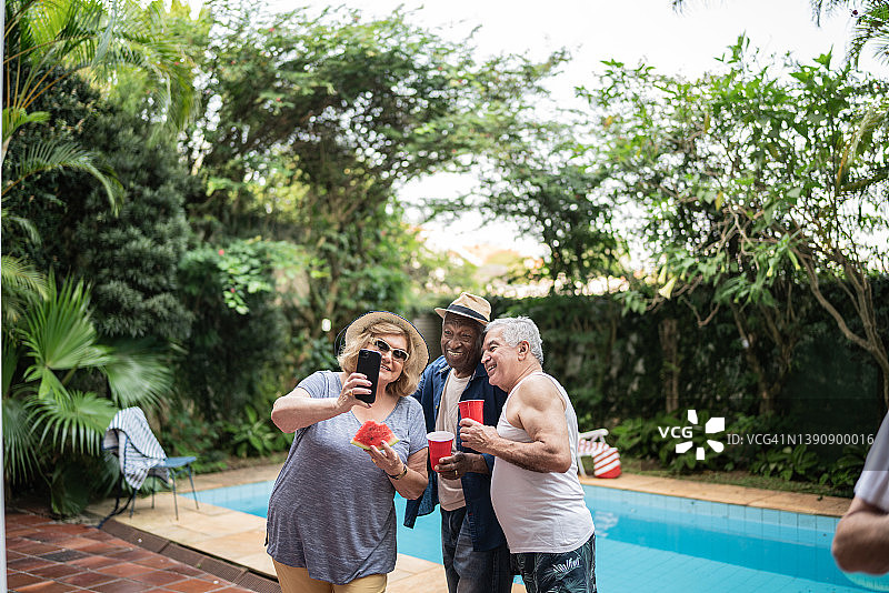 老年朋友在泳池派对上用手机自拍图片素材