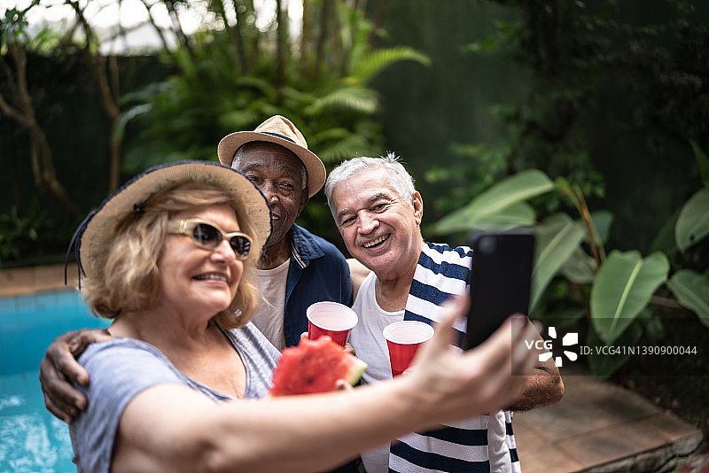 老年朋友在泳池派对上用手机自拍图片素材