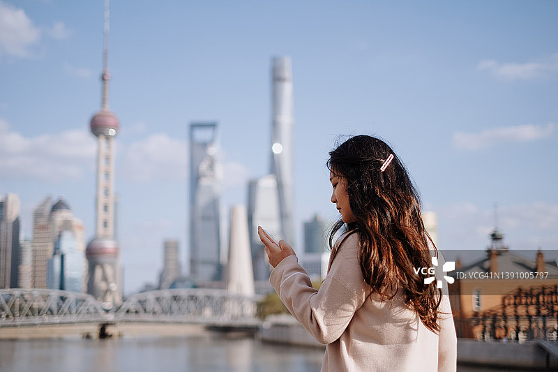 自信的亚洲女性在中国上海金融区使用智能手机图片素材