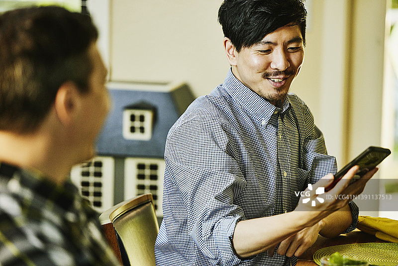 微笑的男人在与家人的晚餐中看智能手机图片素材