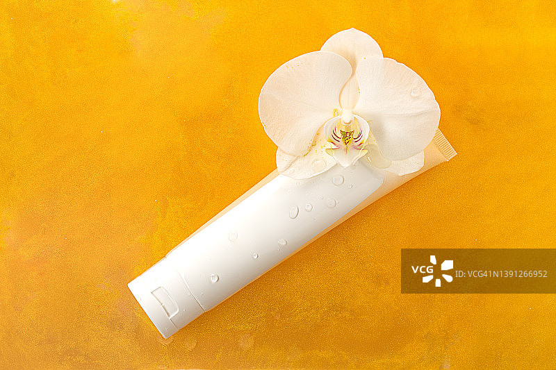 白色软管面霜或护手霜和橙色液体质地中的白色兰花图片素材
